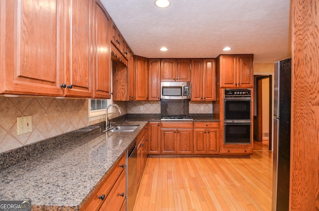 kitchen featuring sink, tasteful backsplash, stone counters, stainless steel appliances, and light hardwood / wood-style floors