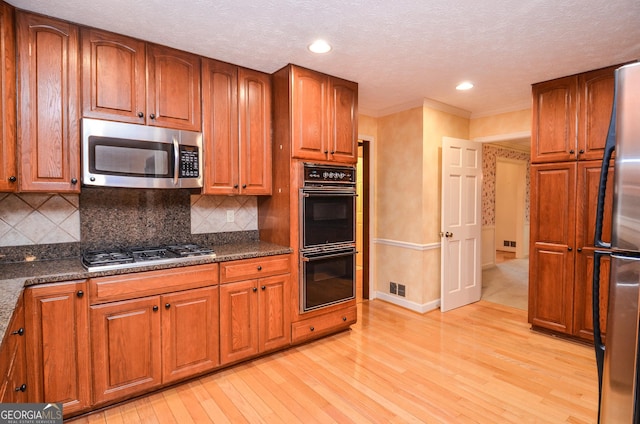 kitchen with stainless steel appliances, light hardwood / wood-style flooring, and dark stone counters