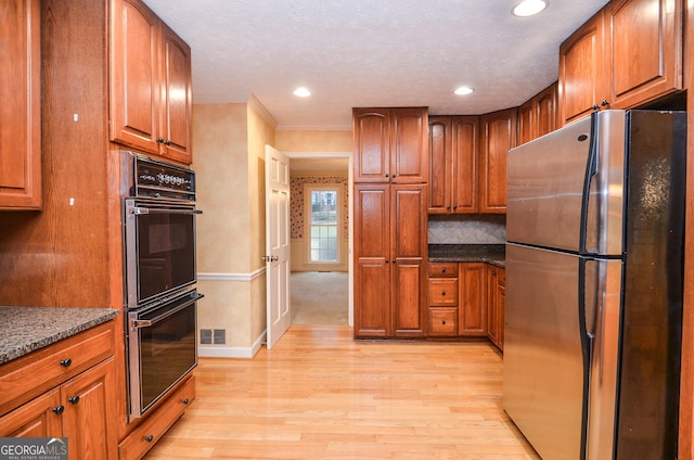 kitchen with stainless steel refrigerator, tasteful backsplash, dark stone counters, black double oven, and light hardwood / wood-style floors