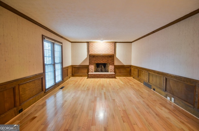 unfurnished living room featuring a fireplace, ornamental molding, and light wood-type flooring