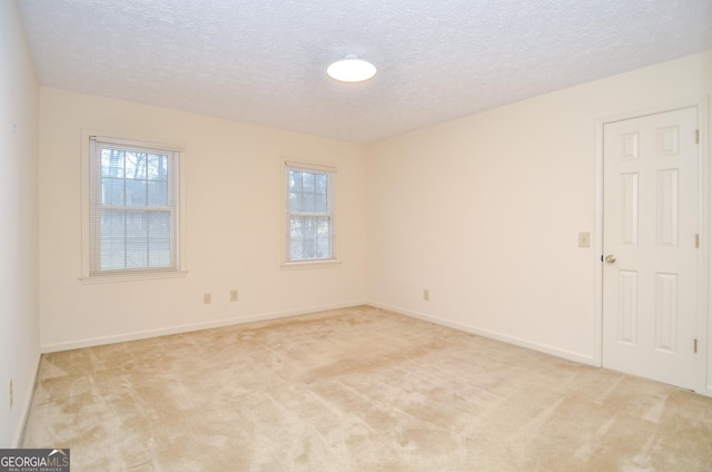 spare room with a textured ceiling, light colored carpet, and a healthy amount of sunlight