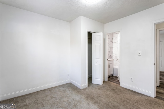 unfurnished bedroom with carpet floors, a closet, ensuite bathroom, a textured ceiling, and baseboards