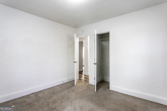 unfurnished bedroom with a closet, light colored carpet, a textured ceiling, and baseboards