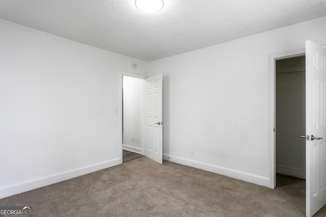 unfurnished bedroom with carpet floors, a walk in closet, a textured ceiling, and baseboards