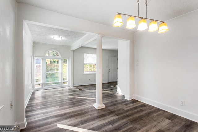 unfurnished dining area with dark wood-style flooring, baseboards, a textured ceiling, and ornate columns