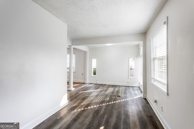 interior space featuring ornate columns, a textured ceiling, baseboards, and wood finished floors