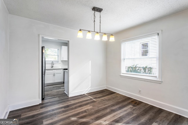 unfurnished dining area featuring a textured ceiling, dark wood-type flooring, visible vents, and baseboards