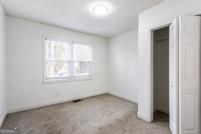 unfurnished bedroom with visible vents, baseboards, carpet, a textured ceiling, and a closet