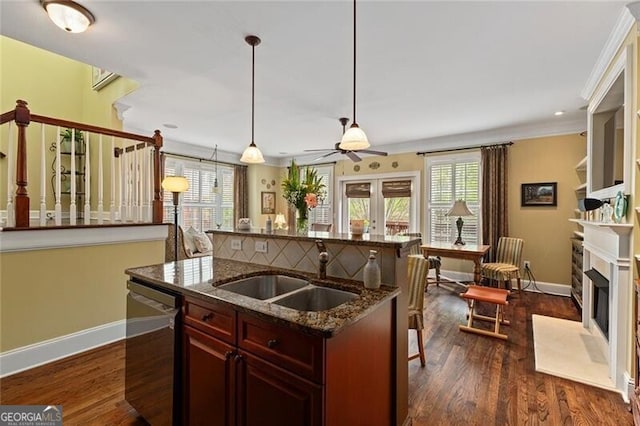 kitchen featuring decorative light fixtures, sink, dark stone countertops, stainless steel dishwasher, and dark wood-type flooring