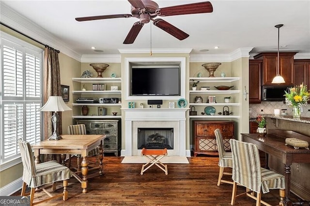 living area featuring crown molding, dark wood-type flooring, a large fireplace, and ceiling fan