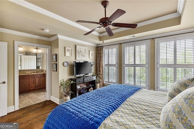 bedroom with wood-type flooring, ornamental molding, connected bathroom, and a tray ceiling