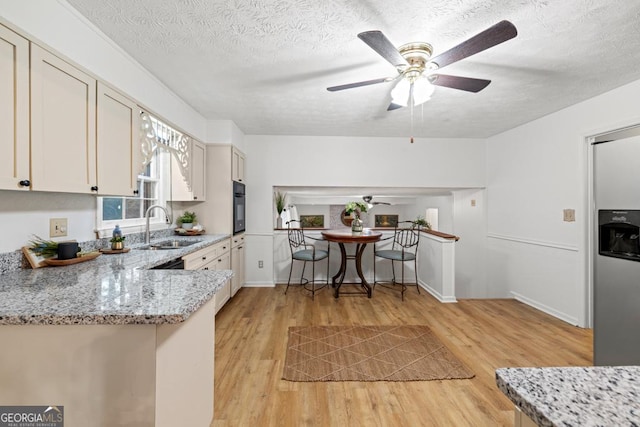 kitchen featuring sink, black oven, light stone counters, and light hardwood / wood-style flooring