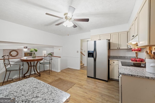 kitchen featuring light wood-type flooring, black electric cooktop, stainless steel fridge, ceiling fan, and cream cabinetry