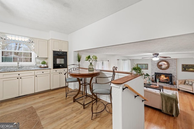 kitchen featuring sink, oven, light stone counters, a brick fireplace, and light hardwood / wood-style flooring