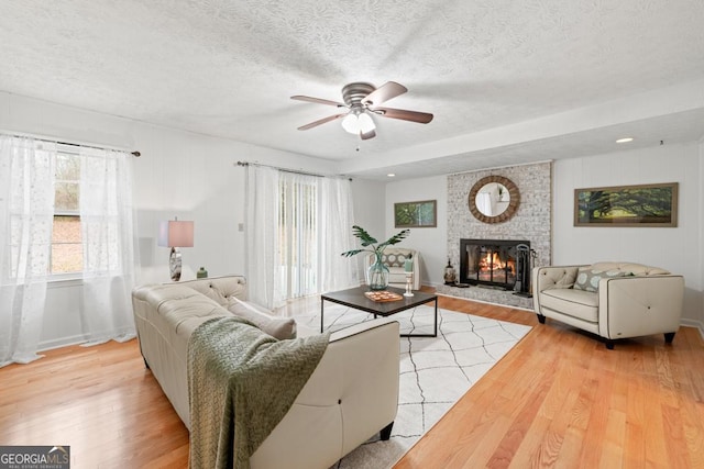 living room with ceiling fan, a brick fireplace, a textured ceiling, and light hardwood / wood-style flooring