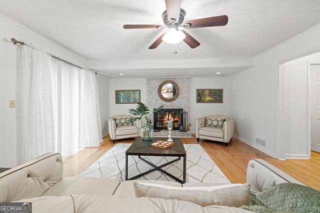 living room with ceiling fan, a brick fireplace, a textured ceiling, and light wood-type flooring