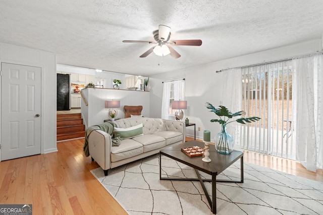 living room featuring ceiling fan, light hardwood / wood-style flooring, and a textured ceiling