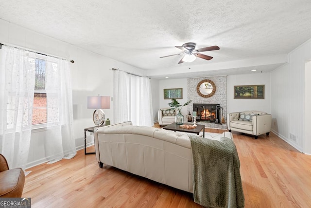 living room featuring ceiling fan, a fireplace, light hardwood / wood-style floors, and a textured ceiling