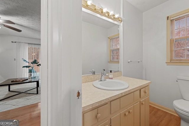 bathroom with hardwood / wood-style flooring, ceiling fan, vanity, a textured ceiling, and toilet