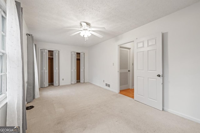 unfurnished bedroom with multiple closets, ceiling fan, light colored carpet, and a textured ceiling