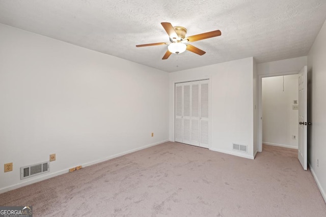 unfurnished bedroom with ceiling fan, a closet, light carpet, and a textured ceiling