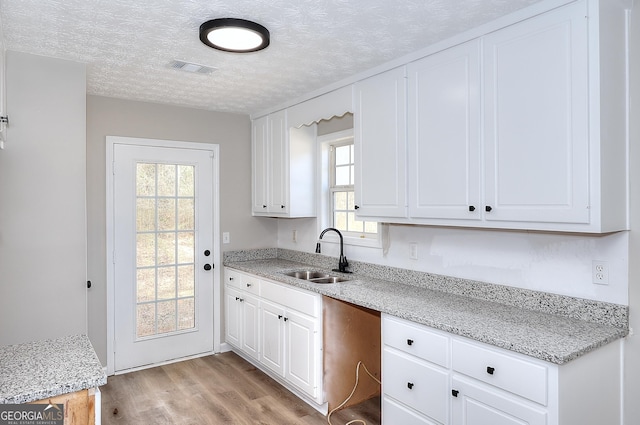 kitchen featuring sink, white cabinetry, a textured ceiling, light stone countertops, and light hardwood / wood-style floors