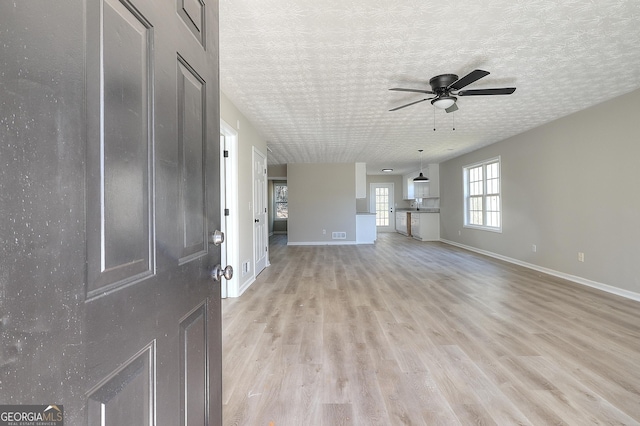 unfurnished living room featuring ceiling fan, a textured ceiling, and light wood-type flooring