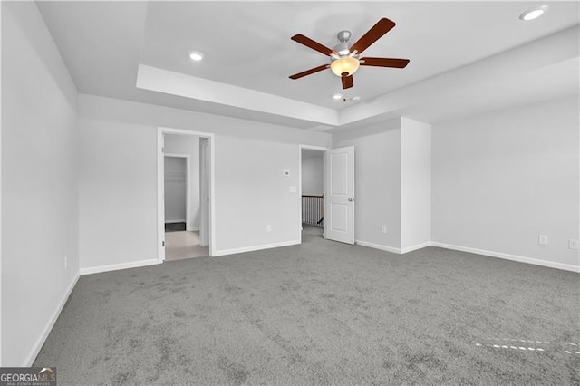 unfurnished bedroom featuring a spacious closet, a raised ceiling, ceiling fan, and carpet flooring