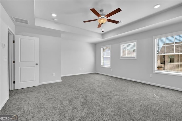 empty room featuring a raised ceiling, carpet flooring, and ceiling fan