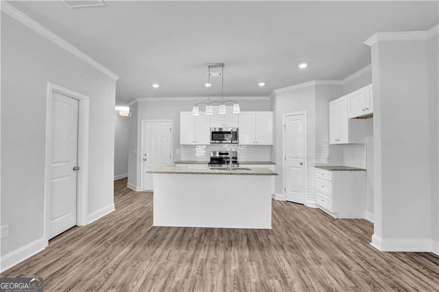 kitchen with appliances with stainless steel finishes, a kitchen island with sink, white cabinetry, light hardwood / wood-style floors, and decorative light fixtures