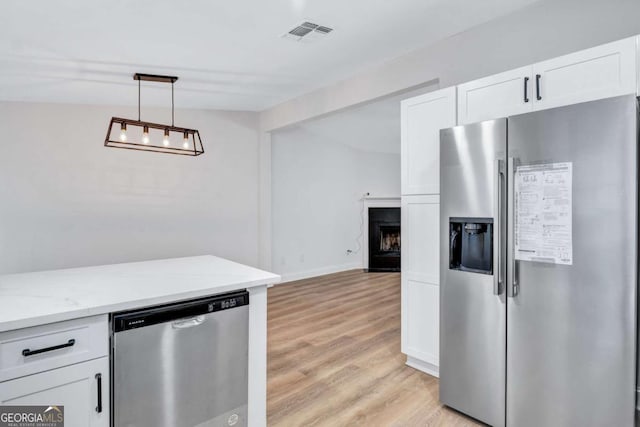 kitchen with appliances with stainless steel finishes, pendant lighting, white cabinetry, light stone countertops, and light hardwood / wood-style flooring