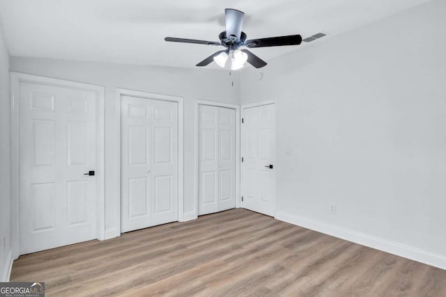 unfurnished bedroom featuring ceiling fan, light hardwood / wood-style floors, and two closets