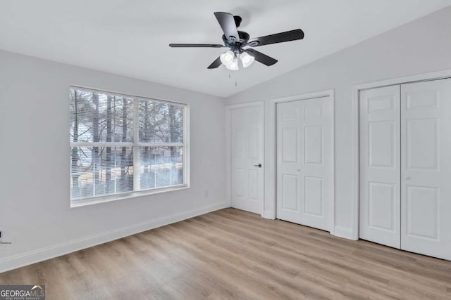 unfurnished bedroom featuring light hardwood / wood-style flooring, ceiling fan, vaulted ceiling, and multiple closets