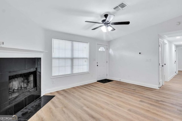 unfurnished living room featuring a tiled fireplace, light hardwood / wood-style flooring, and ceiling fan