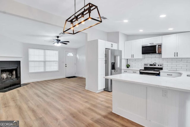 kitchen with white cabinetry, backsplash, hanging light fixtures, stainless steel appliances, and light wood-type flooring