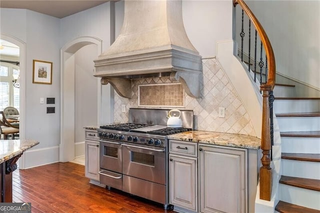 kitchen with premium range hood, double oven range, light stone counters, tasteful backsplash, and dark hardwood / wood-style flooring