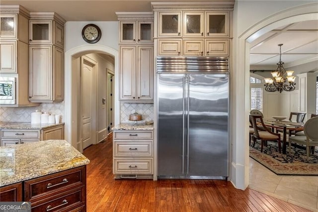 kitchen with built in appliances, dark wood-type flooring, light stone countertops, and cream cabinetry