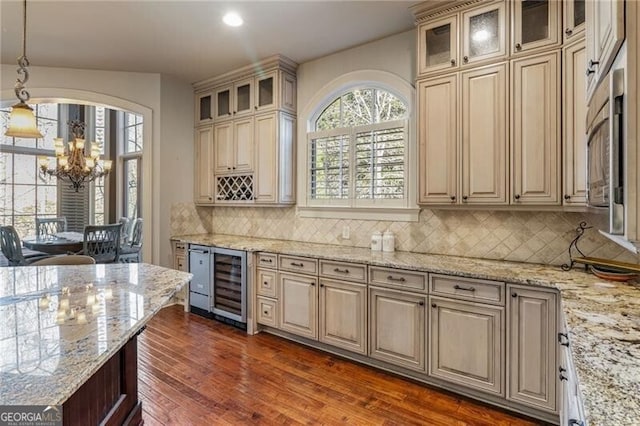 kitchen with wine cooler, light stone counters, cream cabinets, and hanging light fixtures