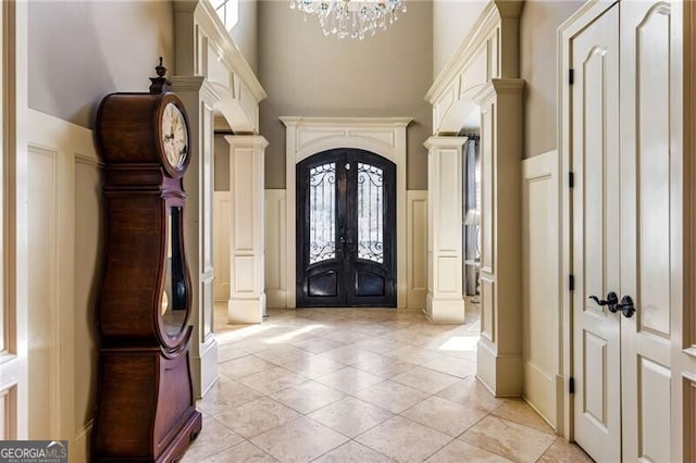 entrance foyer with ornate columns, light tile patterned floors, an inviting chandelier, and french doors