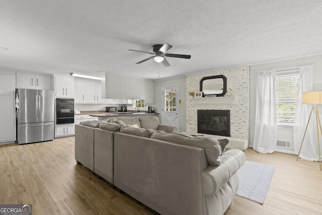 living room featuring light hardwood / wood-style flooring, ceiling fan, ornamental molding, a textured ceiling, and a brick fireplace