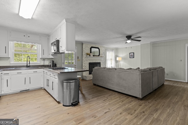 kitchen featuring a fireplace, stainless steel gas stovetop, white cabinetry, sink, and kitchen peninsula