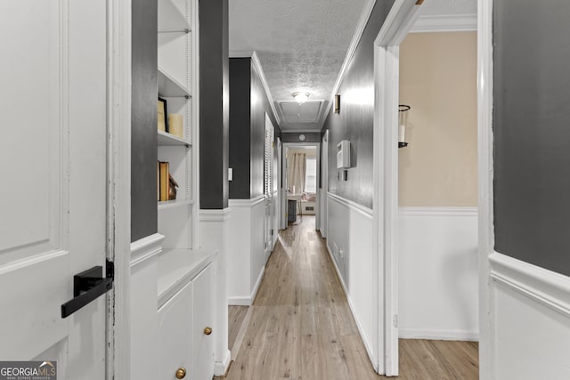 hall with crown molding, built in features, light hardwood / wood-style floors, and a textured ceiling