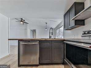 kitchen with appliances with stainless steel finishes, sink, wall chimney range hood, and light hardwood / wood-style flooring