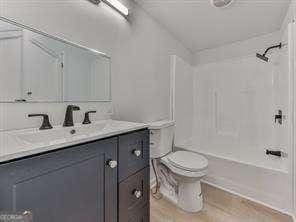 full bathroom with hardwood / wood-style flooring, vanity, shower / bathing tub combination, vaulted ceiling, and toilet