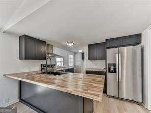 kitchen featuring sink, light hardwood / wood-style floors, kitchen peninsula, stainless steel refrigerator with ice dispenser, and wall chimney range hood