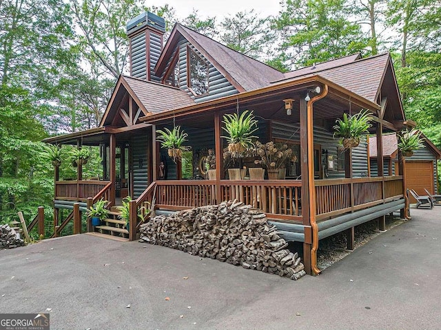 view of front of property with covered porch, a shingled roof, and faux log siding