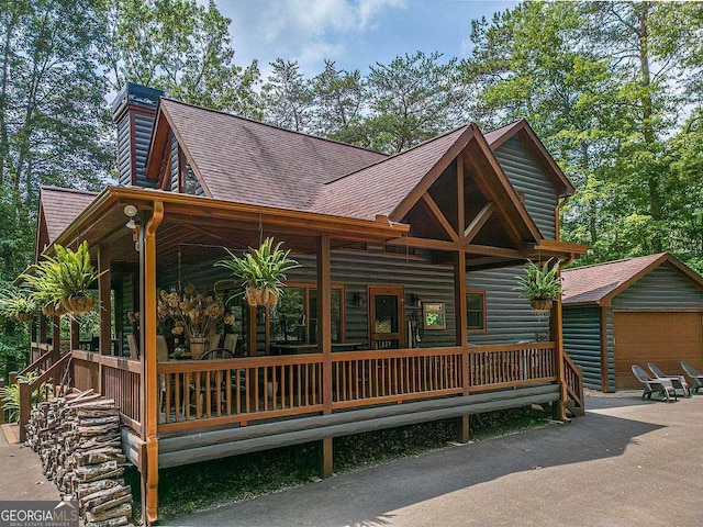 view of front of property featuring an outbuilding, a porch, a garage, roof with shingles, and log veneer siding