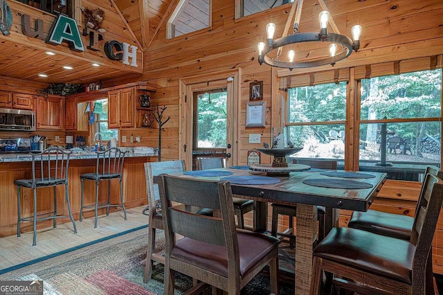 dining space featuring wood ceiling, an inviting chandelier, high vaulted ceiling, wood walls, and light wood-type flooring