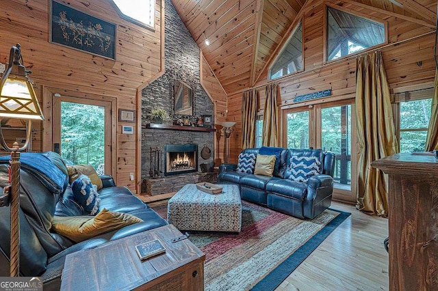 living room with a stone fireplace, wood walls, wood ceiling, high vaulted ceiling, and light hardwood / wood-style flooring