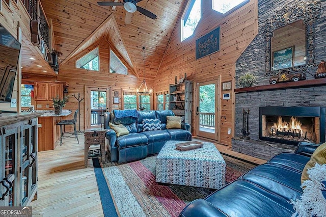 living room featuring wooden walls, wooden ceiling, ceiling fan, light wood-type flooring, and a fireplace